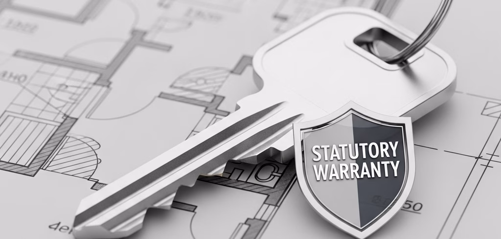 A silver house key resting on a building blueprint, with a small shield emblem attached that is labeled "STATUTORY WARRANTIES." This image symbolizes the mandatory legal STATUTORY WARRANTIES and protection for residential construction work in NSW under the Home Building Act.